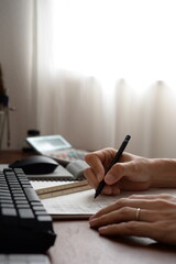 Fototapeta premium Architect writing design notes at desk with keyboard and calculator キーボードと電卓のあるデスクで設計メモを書く建築士の手元