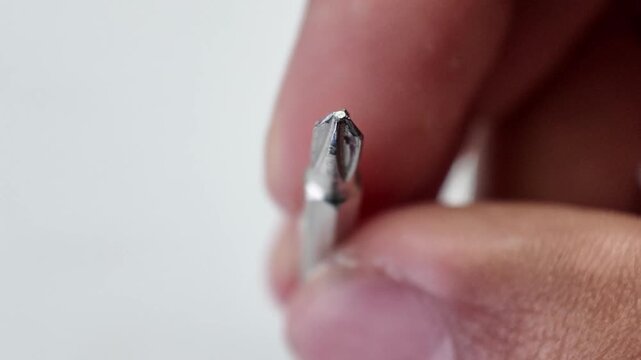 Close up shot of a hand gathering an assortment of scattered steel screwdriver bits into a neat group pile on a gray background.