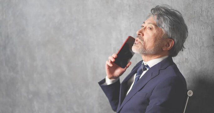 赤いスマートフォンを操作する50代のエグゼクティブ男性