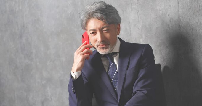 赤いスマートフォンを操作する50代のエグゼクティブ男性