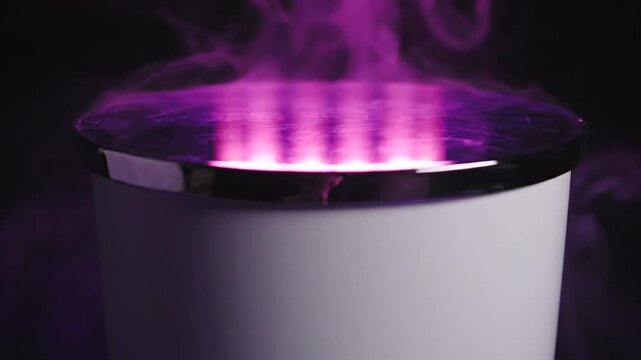A white cylindrical pedestal with a silver metallic rim emitting dense purple and pink smoke and vapor that flows over the edges and around the base against a solid black background.