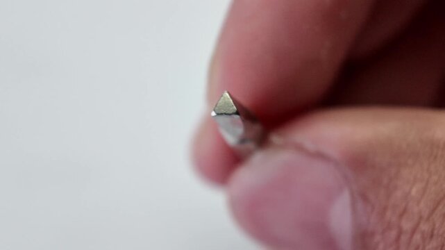 Detailed macro shot of a person's fingers dropping a silver magnetic extension bit holder tool onto a gray surface background.