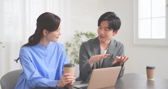 ノートパソコンの前でコーヒーを飲みながら話し合うカップル