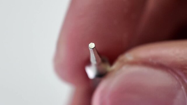 Top down macro shot of human fingers placing a magnetic hex socket nut driver bit tool onto a flat gray workspace surface.