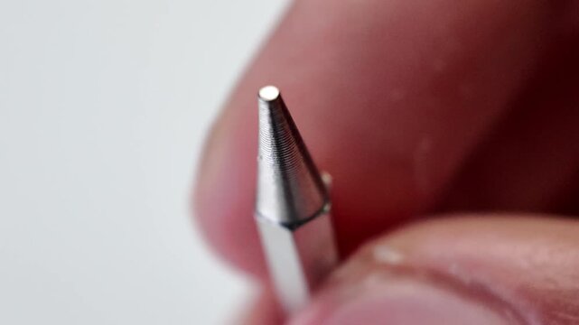 Detailed macro shot of a person's hand carefully placing a silver pozidriv cross head screwdriver bit down onto a neutral grey backdrop sheet.