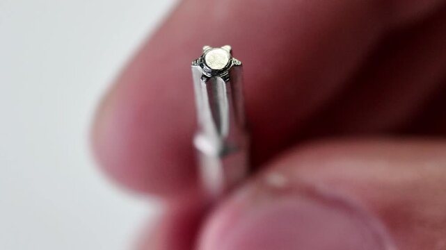 Macro view of a technician's hand lifting a long steel square drive robertson screwdriver bit from a clean gray paper studio surface background.