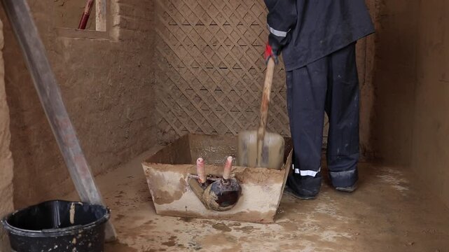 A builder mixes cement mortar indoors during plastering work. A close-up of the tools and the process of preparing the mixture.