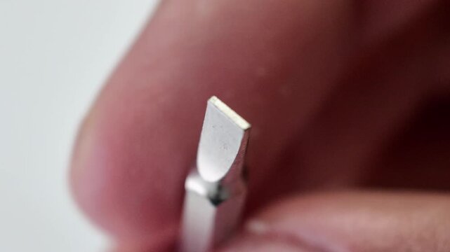 Close up shot of fingers picking up a long metallic star shaped torx security screwdriver bit tool from a plain gray workbench paper.