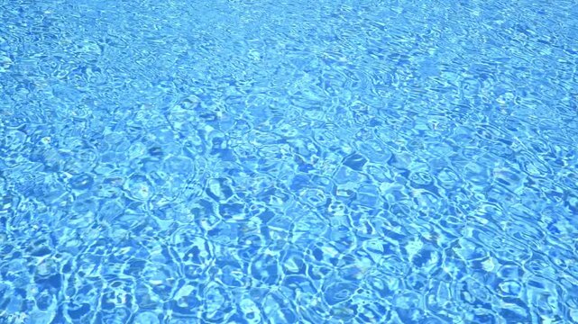 Sunlight reflects on the rippling water surface of a swimming pool, creating a mesmerizing pattern of light and shadow in vibrant shades of blue, perfect for summer backgrounds and travel themes