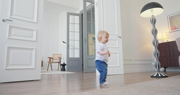 Blond toddler exploring a bright modern living room with wooden floors, tall patterned floor lamp, open doors, and cozy contemporary furniture