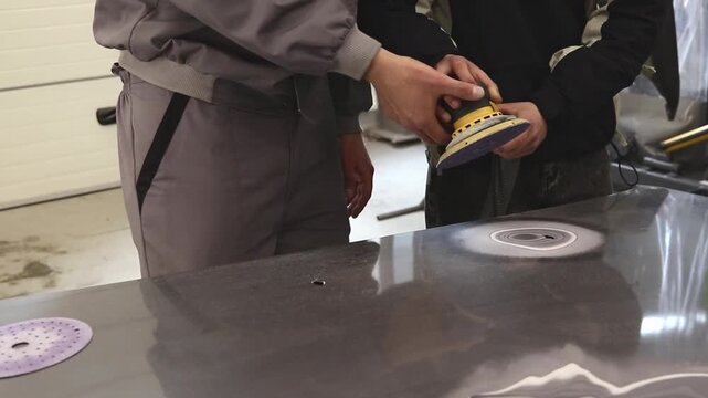 Close-up of a craftsman removing defects from a car body using an orbital sander. Preparing the hood of a car for painting.