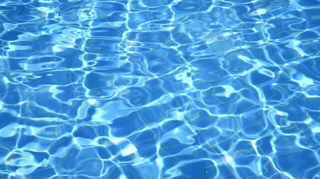 Sunlight reflects on the rippling water surface of a swimming pool, creating a mesmerizing pattern of light and shadow in vibrant shades of blue, perfect for summer backgrounds and travel themes