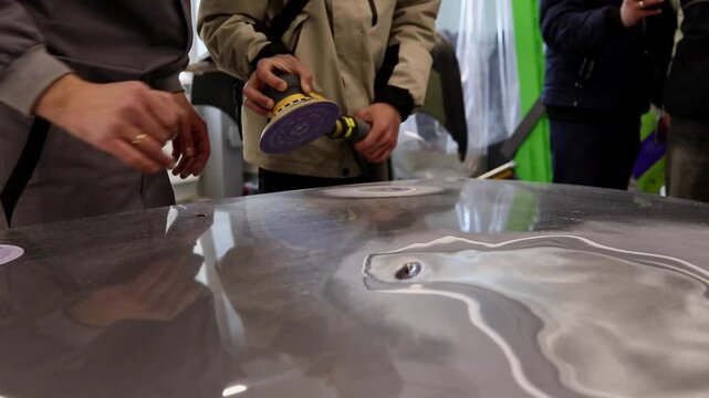 A craftsman polishes a car hood in a body shop while preparing a car for painting and repair.