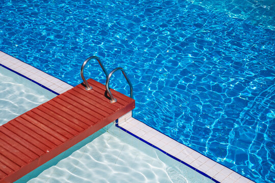 Sunlight shimmering on the rippling surface of a swimming pool, with grab bars and a wooden deck offering easy access for swimmers seeking relaxation and enjoyment in a tropical paradise