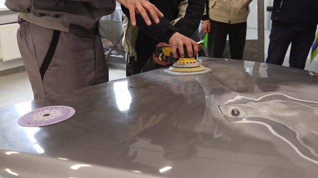 Close-up of the work process of grinding the hood of a car. Students are studying in a workshop for the repair and restoration of car bodies.