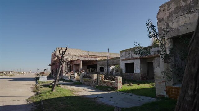 A street-level view of the desolate, abandoned concrete ruins and dead trees lining a paved road in the famous ghost town of Villa Epecu&eacute;n, Argentina.
