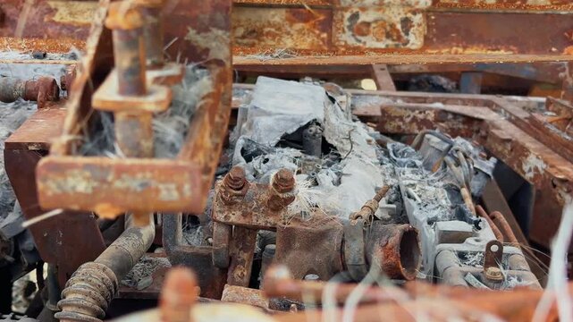 Tracking shot of damaged engine components inside a fire destroyed sleeper bus showing rusted mechanical parts, melted materials and ash covered metal framework!
