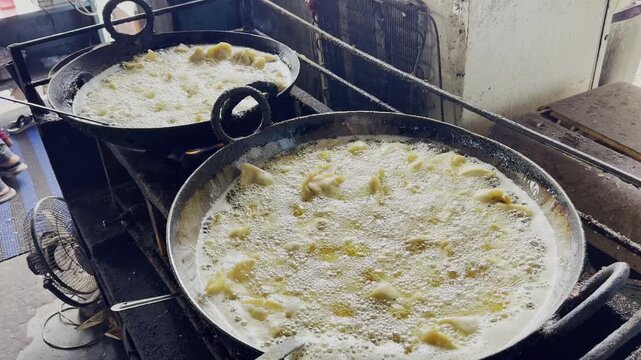Traditional samosas being deep fried in large iron kadais filled with bubbling hot oil inside a busy Indian street food kitchen!