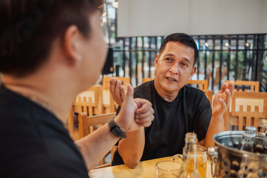 Young man politely goes along with his slightly intoxicated friend's exaggerated stories and bold claims during a casual conversation at a bar.