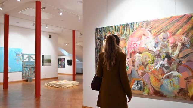 Woman viewing large contemporary oil painting in modern art gallery exhibition.