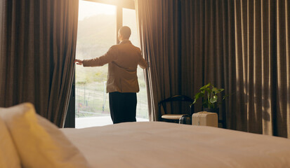 Fototapeta premium Man, sunlight and open curtain in hotel room for window view to start day, fresh air and relax. Business trip, accommodation and person at lodge with luggage, back and bedroom for hospitality