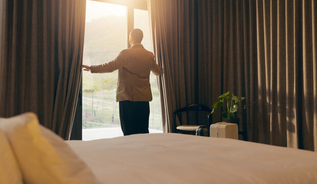 Man, sunlight and open curtain in hotel room for window view to start day, fresh air and relax. Business trip, accommodation and person at lodge with luggage, back and bedroom for hospitality