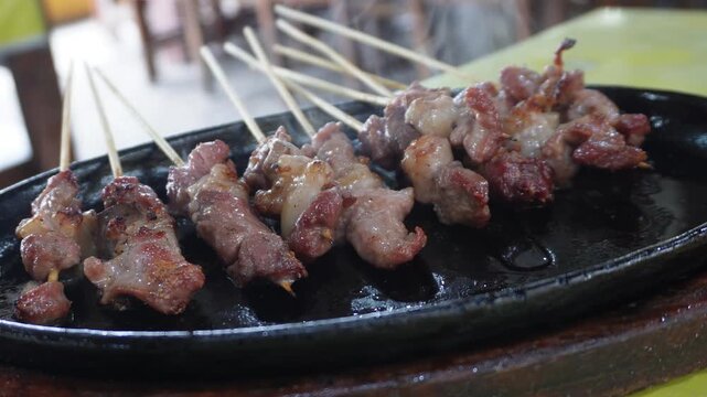 Delicious Sate Klathak, a traditional mutton satay from Yogyakarta, served hot and sizzling on a black hotplate, close-up view.