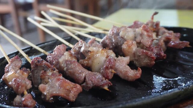 Delicious Sate Klathak, a traditional mutton satay from Yogyakarta, served hot and sizzling on a black hotplate, close-up view.