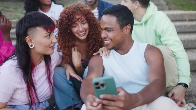 Young multiracial group of friends using mobile smartphone sitting outside of college - Youth people lifestyle concept - Focus on nonbinary african person