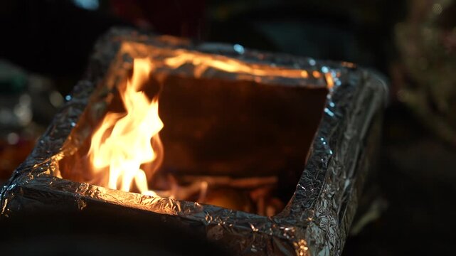Bright orange flames dance within a square metal container during a traditional spiritual ceremony captured in this evocative close up photograph.