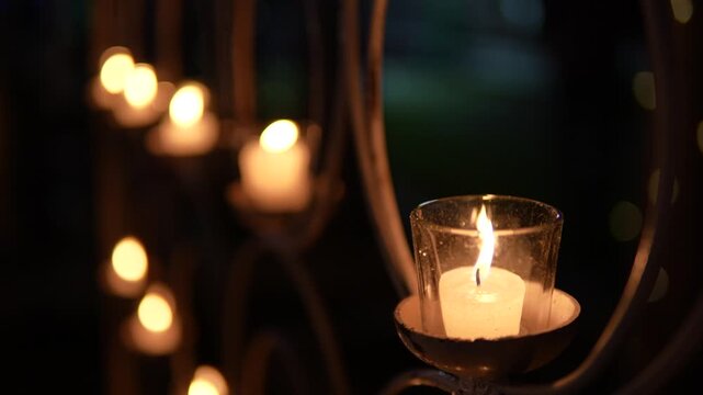 Small glowing candle rests inside a clear glass holder providing soft warm light in a beautiful peaceful night photograph scene.