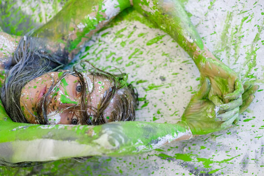 Close portrait of young woman covered in vivid green paint splashes looking through raised arms dynamic body art composition with expressive texture bold color and intense gaze