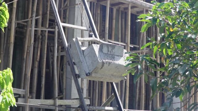 Concrete lift bucket tipping wet cement into a pouring funnel system at a construction site against blue sky.