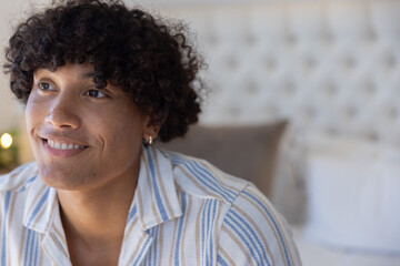 Adult male smiling, looking upward while sitting on bed with striped shirt and hoop earring © wavebreak3