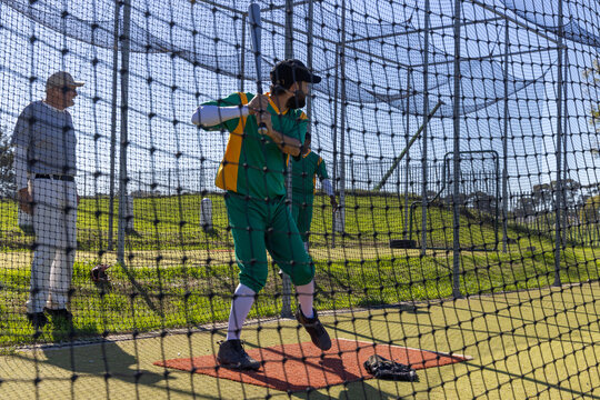 Coach signaling pitch, baseball batter practicing swing on red mat with bat, net and glove visible