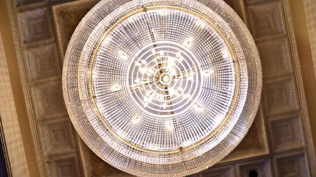 Large crystal chandelier illuminates an ornate ceiling with brilliant light in this impressive photograph of a sophisticated interior design element.