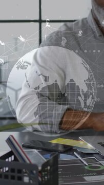 Vertical video: Man entering, touching laptop, doing finance work while globe hovering over laptop
