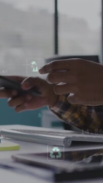 Vertical video: Man tapping smartphone summoning eco icons then typing on keys logging green data