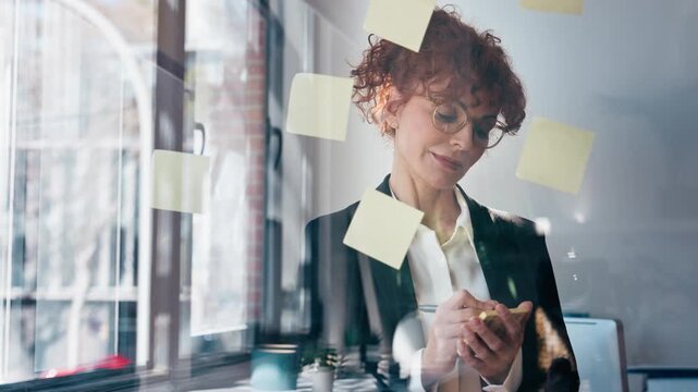 Video of elegant business woman working on wall glass with notes stickers in the office