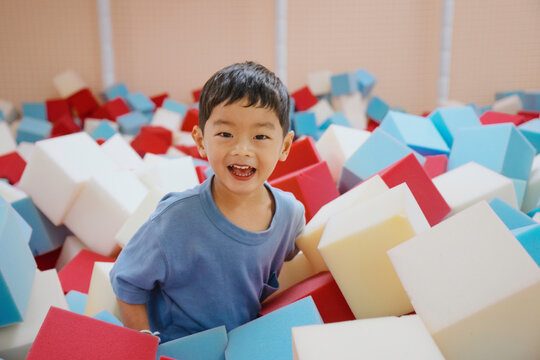 Smiling young Asian boy playing with colorful foam blocks in indoor playground or kids club. Fun educational activity for child development, learning and recreation concepts.