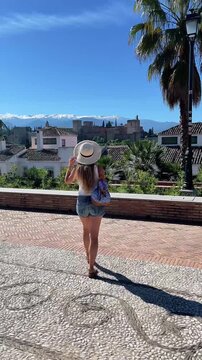 Tourist woman looking at Alhambra palace and sierra nevada mountain from a viewpoint in Granada, Travel in Spain, Europe