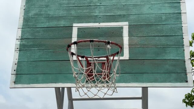 Old outdoor basketball hoop on a green wooden backboard under a clear blue sky. Tilt up shot sunny day