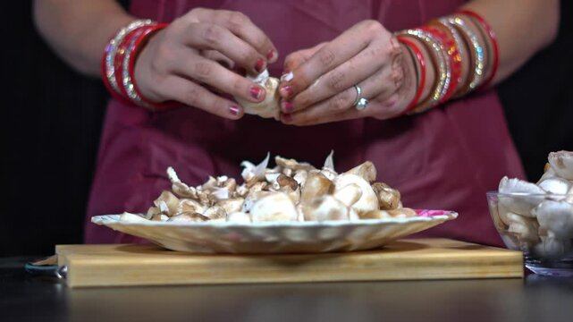 Indian woman hands peeling and breaking fresh white mushrooms into a plate. 