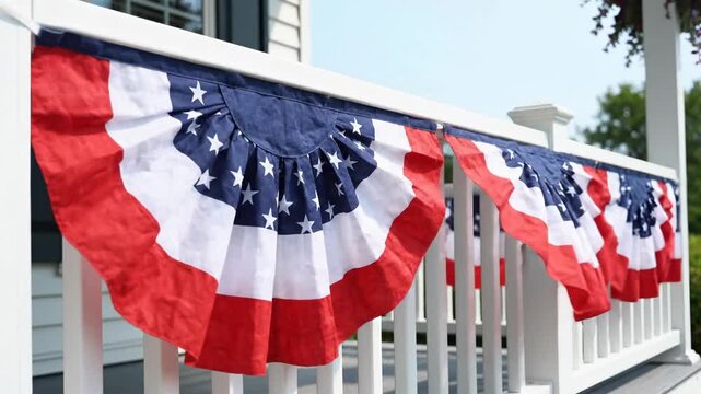 Patriotic American flag bunting hanging on a white wooden porch railing. Red white and blue pleated fans decorating a home for the Fourth of July