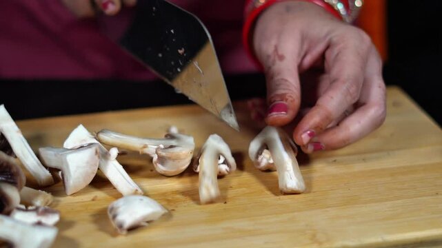 Indian woman hands chopping fresh white mushrooms with kitchen cleaver knife