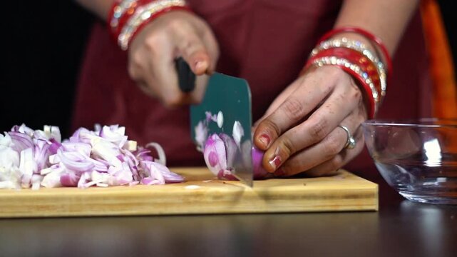 Indian woman hands slicing red onion on wooden board for cooking. Close up of South Asian housewife chopping red onion with sharp knife.
