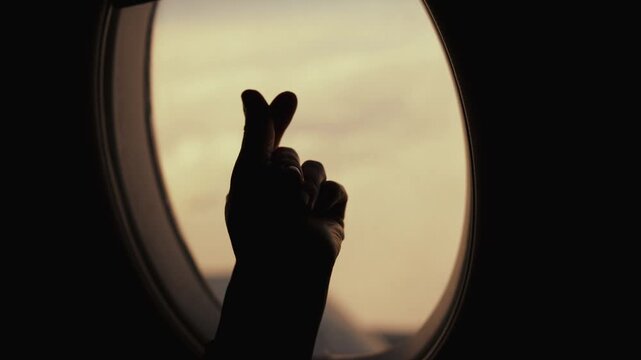 Love to travel in flight by plane, silhouette of human hand showing heart symbol . Happy and inspired passenger showing heart by fingers against airplane window, enjoy summer holidays and vacation