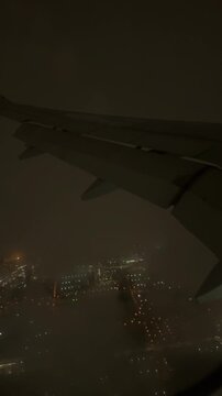 Passenger's view from airplane window during night landing over a city with low clouds and clouds illuminated by city lights, creating a dramatic and beautiful urban nightscape