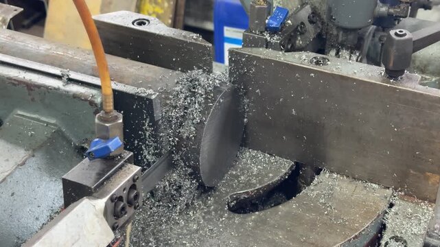 Metalworking machine operates in a factory, shaping steel with spinning tools amid industrial noise and coolant spray.