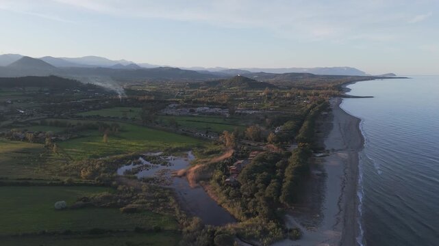 Extended sandy coastline at Spiaggia di Perd'e Pera Sardinia with calm sea and rural surroundings, drone